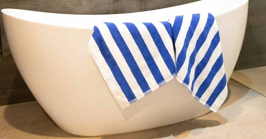 Blue and white striped towels draped over a freestanding white bathtub